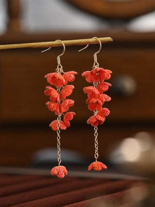 Red floral earrings on a wooden stick with a blurred background
