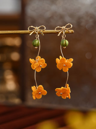 Pair of orange floral earrings with green beads on a blurred background