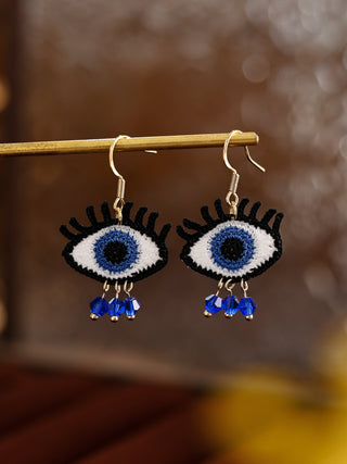 Eyeball-shaped earrings with blue accents on a blurred background