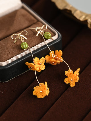 Orange flower-shaped earrings with green beads on a brown surface