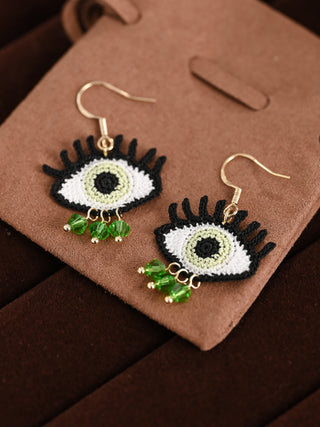 Eye-shaped earrings with green accents on a brown surface