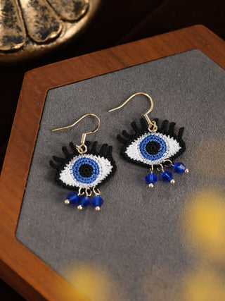 Pair of eye-shaped earrings with blue and black details on a gray surface.
