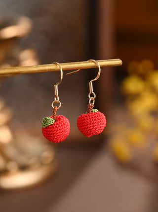 Red crochet earrings on a gold stand with a blurred background