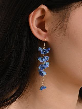 Close-up of a person wearing blue floral earrings with a neutral background