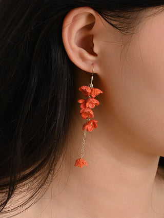 Close-up of an ear wearing a pair of orange floral earrings with a blurred background.