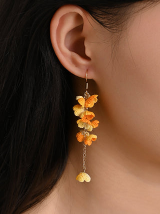Close-up of a person wearing orange floral earrings with a neutral background