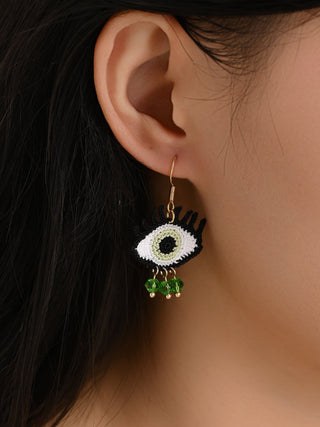 Close-up of an ear wearing a decorative earring with a white center and green beads.