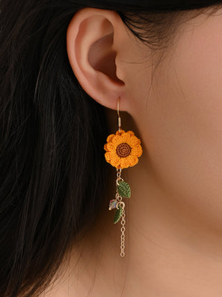 Close-up of a person wearing sunflower-shaped earrings with a chain and leaf detail.