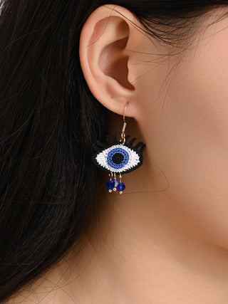 Close-up of an ear wearing a blue and white evil eye earring with a blurred background