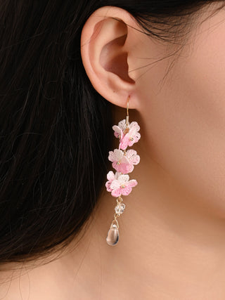 Close-up of a person wearing a floral earring with pink flowers and a small droplet.