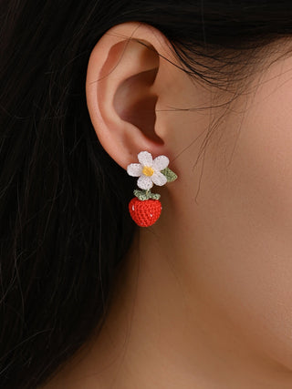 Close-up of an ear wearing a floral earring with a red heart charm.
