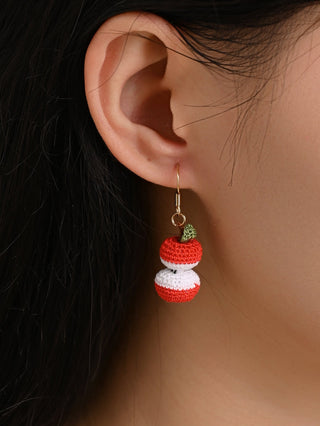 Close-up of an ear wearing an apple-shaped earring with a neutral background