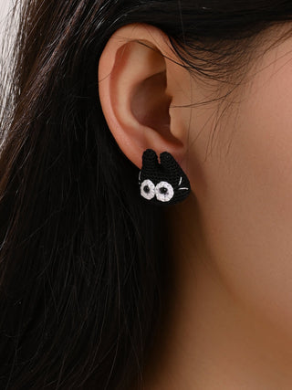 Close-up of a person wearing black cat-shaped earrings with white paws and eyes.