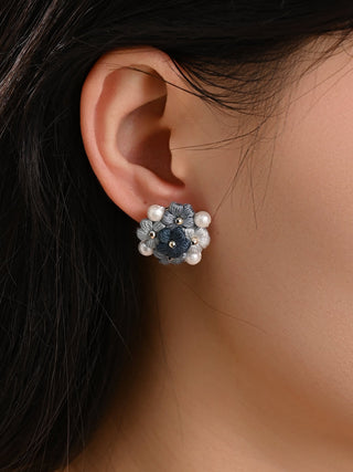 Close-up of an ear wearing a floral earring with blue stones on a neutral background