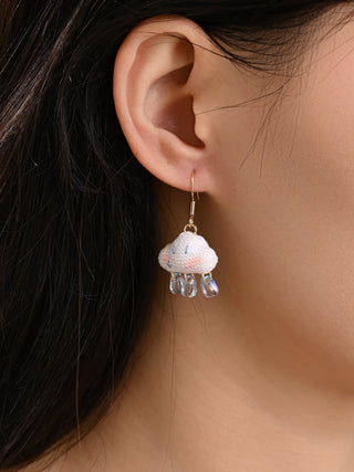 Close-up of a person wearing a floral earring with a clear crystal on a neutral background