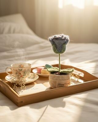Handmade crochet flower in a pot on a breakfast tray with tea, macarons, and a card